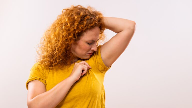 Person checking underarm odor in yellow shirt.
