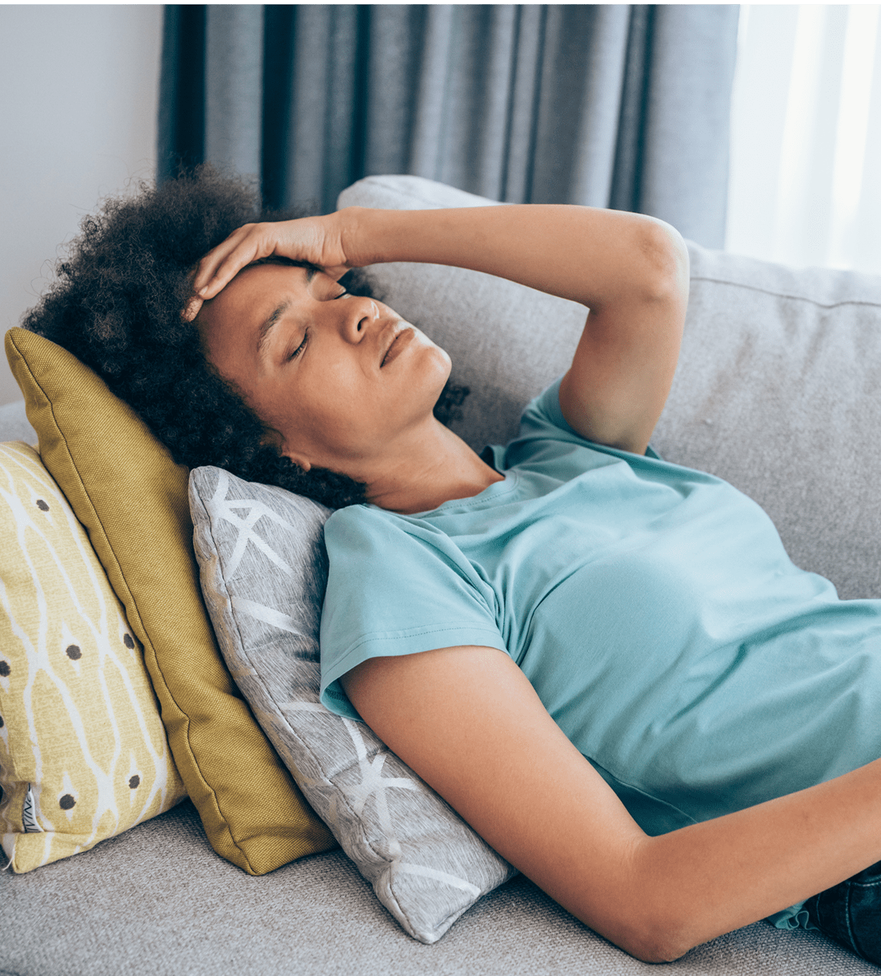 Woman lying on a couch with eyes closed, looking stressed.