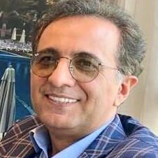 Smiling man wearing glasses and a plaid jacket indoors.